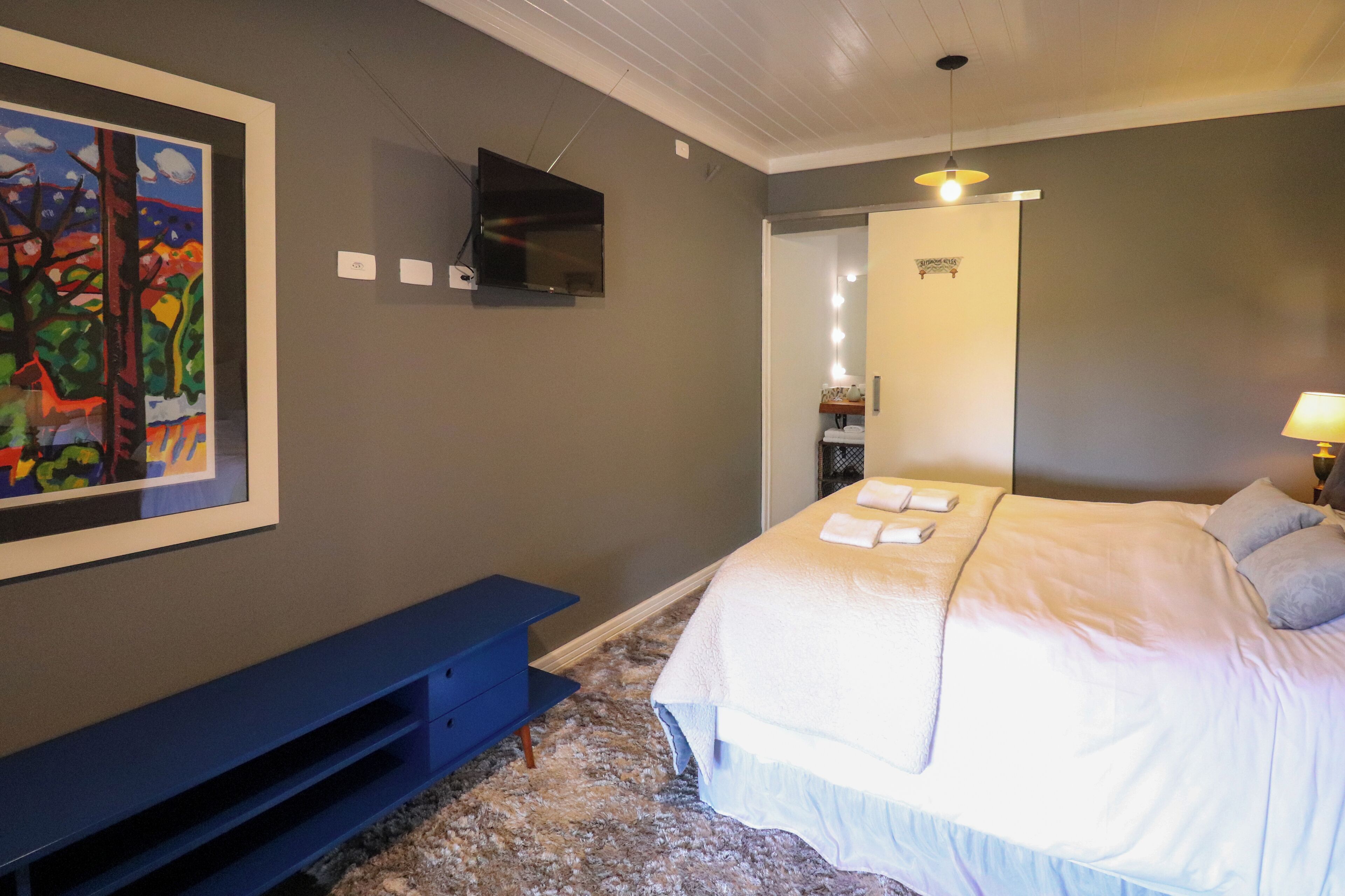 A bedroom with a bed, a bench, a TV, and a painting on the wall.