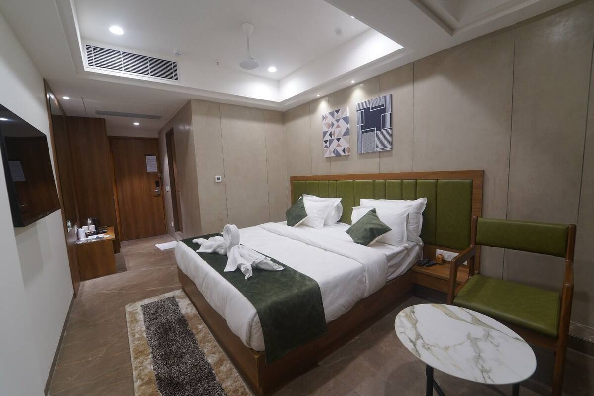 A modern hotel room with a large bed, a green upholstered chair, a small round table, and a ceiling fan.
