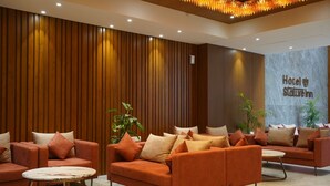 En modern hotellobby med väggar beklädda med träpaneler, orange soffor och en vägg av marmor med hotellets namn.