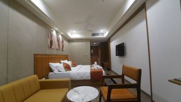 A hotel room with a bed, a sofa, a chair, a small table, a TV mounted on the wall, and a ceiling fan.