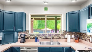 Cucina con mobili blu scuro, lavello in acciaio inossidabile e finestra vista sul verde.