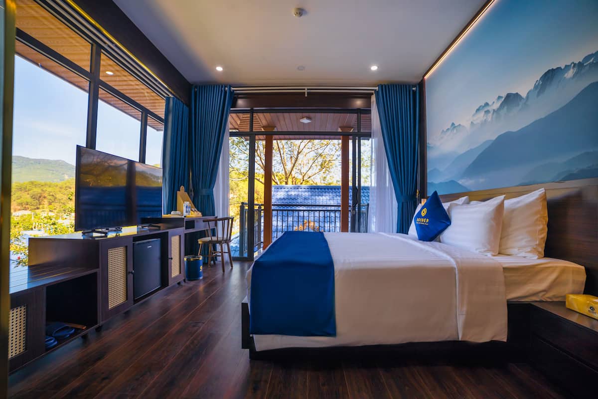 Une chambre d’hôtel moderne dotée d’un grand lit, d’un bureau avec un téléviseur à écran plat et d’un balcon offrant une vue panoramique.