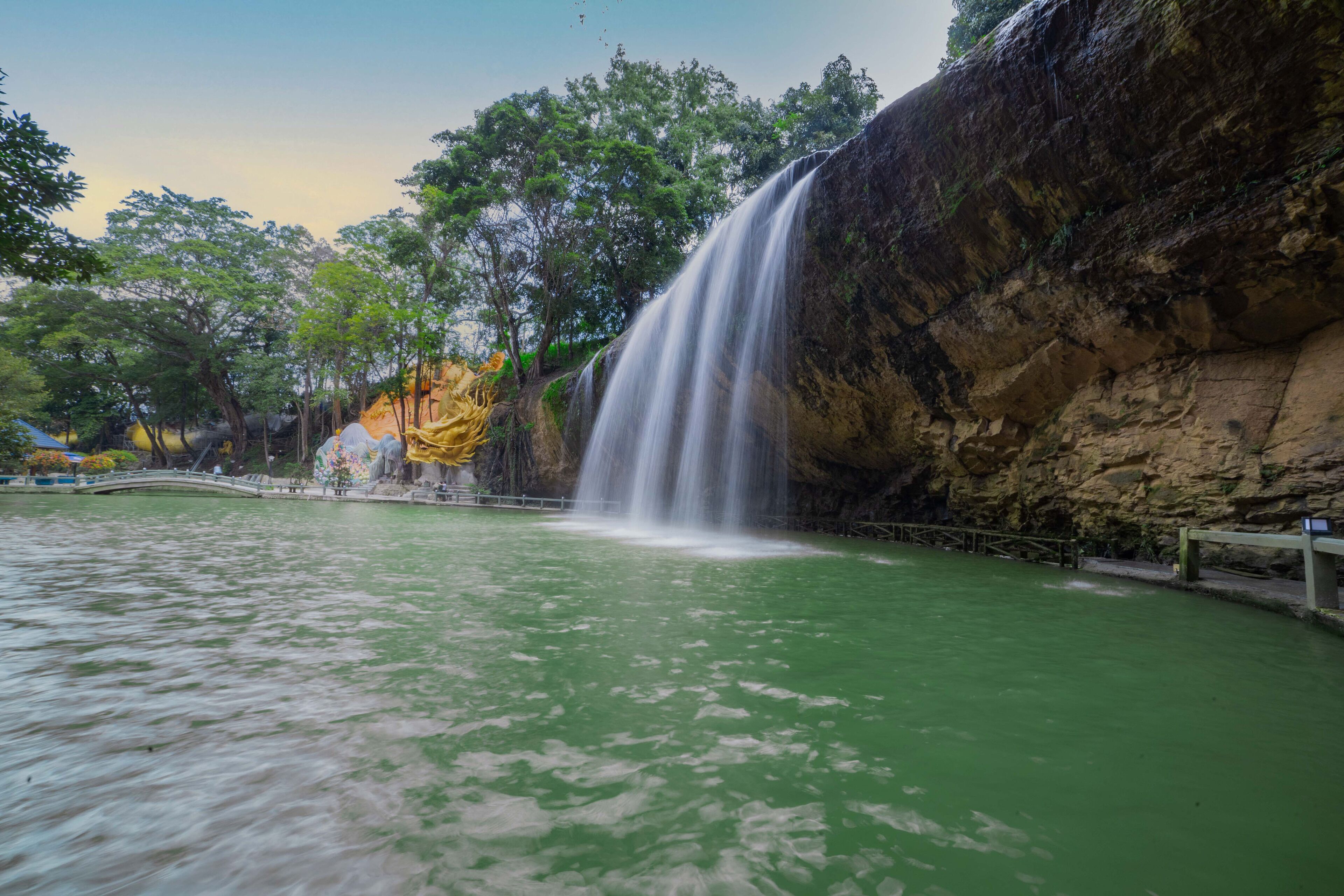 A waterfall cascading into a greenish pool, surrounded by rocky cliffs and trees.