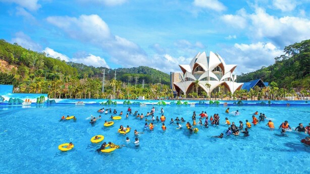 A large swimming pool with people in the water and on the edge, surrounded by a building with a unique architecture. - Tea Resort Prenn (Xuan Huong - Da Lat)
