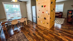 Una habitación con una pared de escalada de madera, una zona de comedor con sillas y una mesa, un refrigerador y un ventilador de techo.