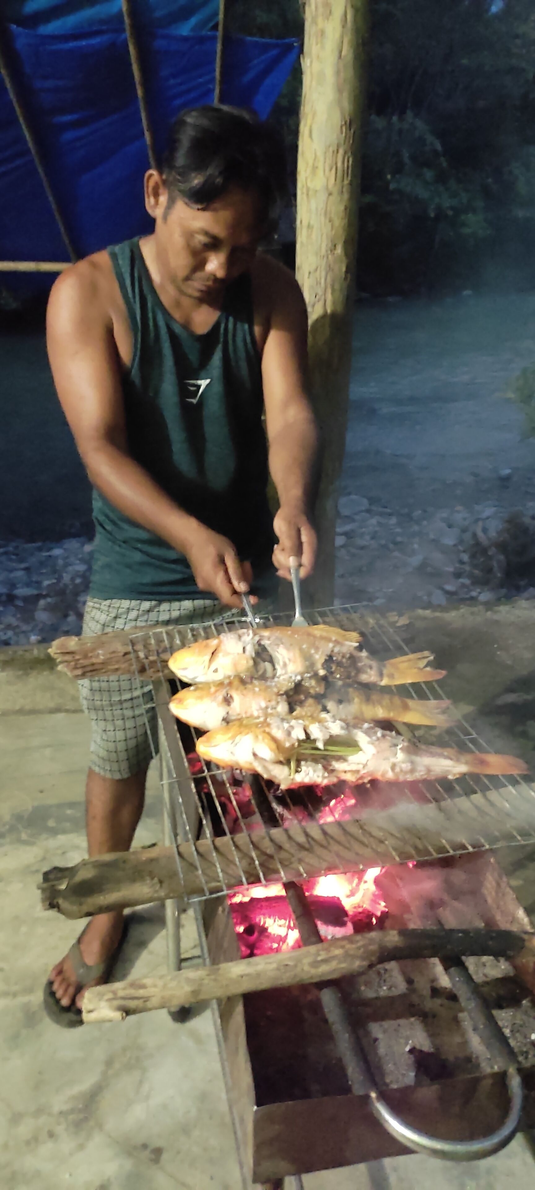 Una persona asando pescado a fuego abierto al aire libre.