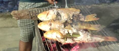 Una persona asando pescado a fuego abierto al aire libre.