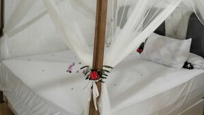 Una cama con dosel y cuatro columnas, con ropa de cama blanca y un arreglo floral.
