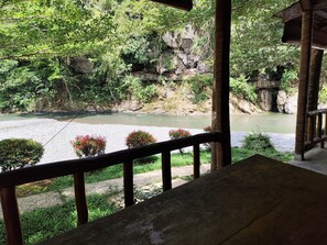A view from a covered area overlooking a river with a rocky cliff and greenery. -  Ibu Bumi Orangutan guesthouse (Bohorok)