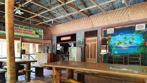 Interior rústico de un restaurante con mesas y bancos de madera, un mural con una escena de selva y un cartel sobre la conservación de tigres.