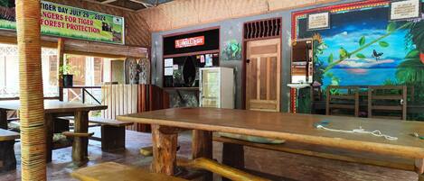 An indoor setting with wooden tables and benches, a sign about tiger conservation, and a mural with frogs and a butterfly.