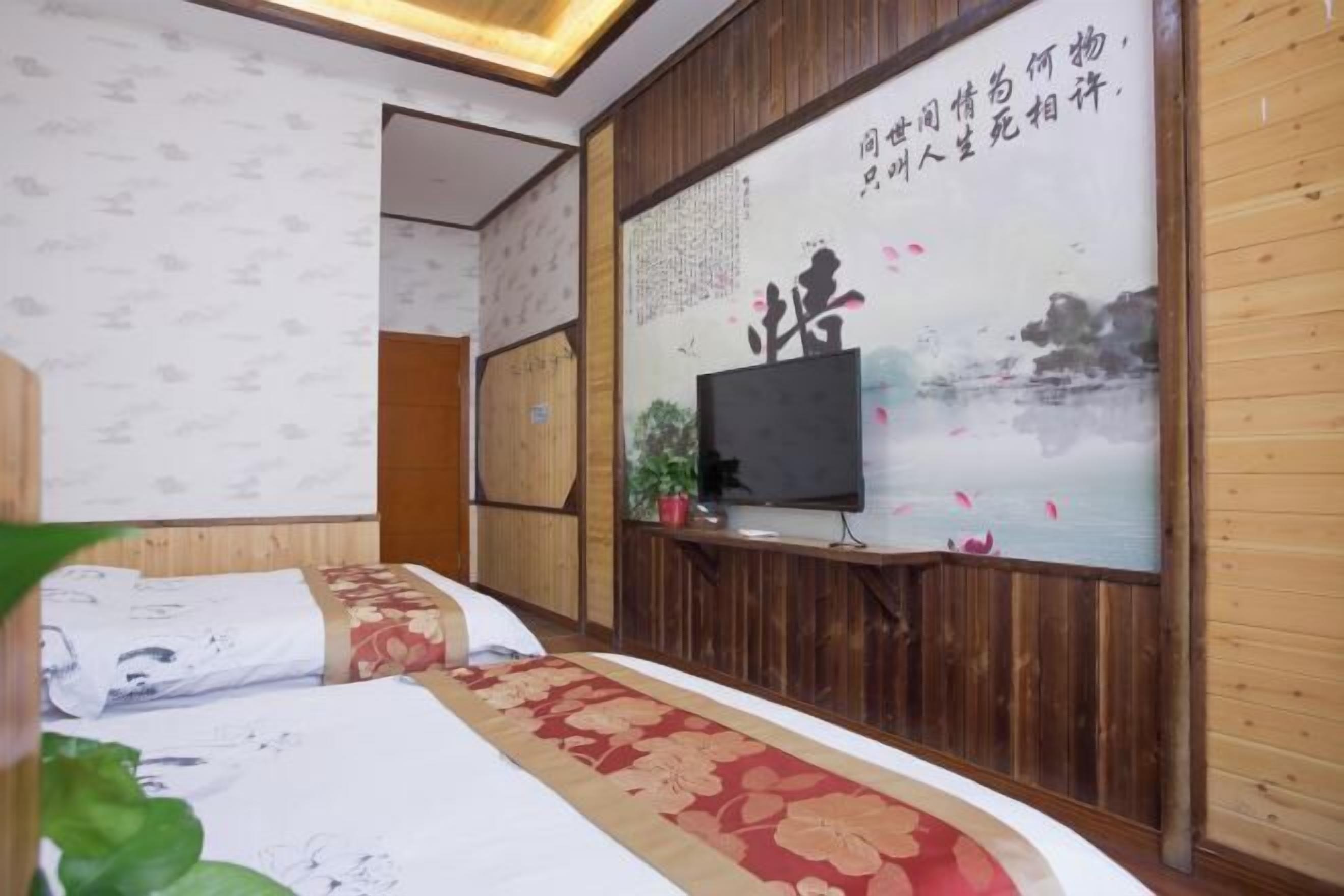 Une chambre d’hôtel avec un mur lambrissé en bois, un lit recouvert d’une couvre-lit à motifs floraux, un téléviseur posé sur un meuble et une affiche ornée de caractères chinois.