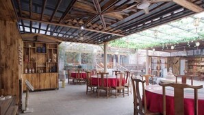 A rustic wooden interior with round tables and chairs, a wooden bar area, and a view through large windows. - Mount Hua Hongchen Xiake Themed Homestay (Huayin)