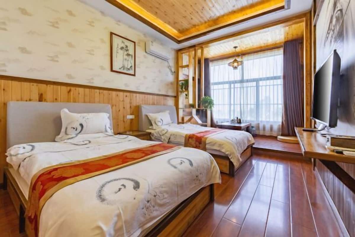 A hotel room with two beds, wooden flooring, a television, and a large window with curtains.