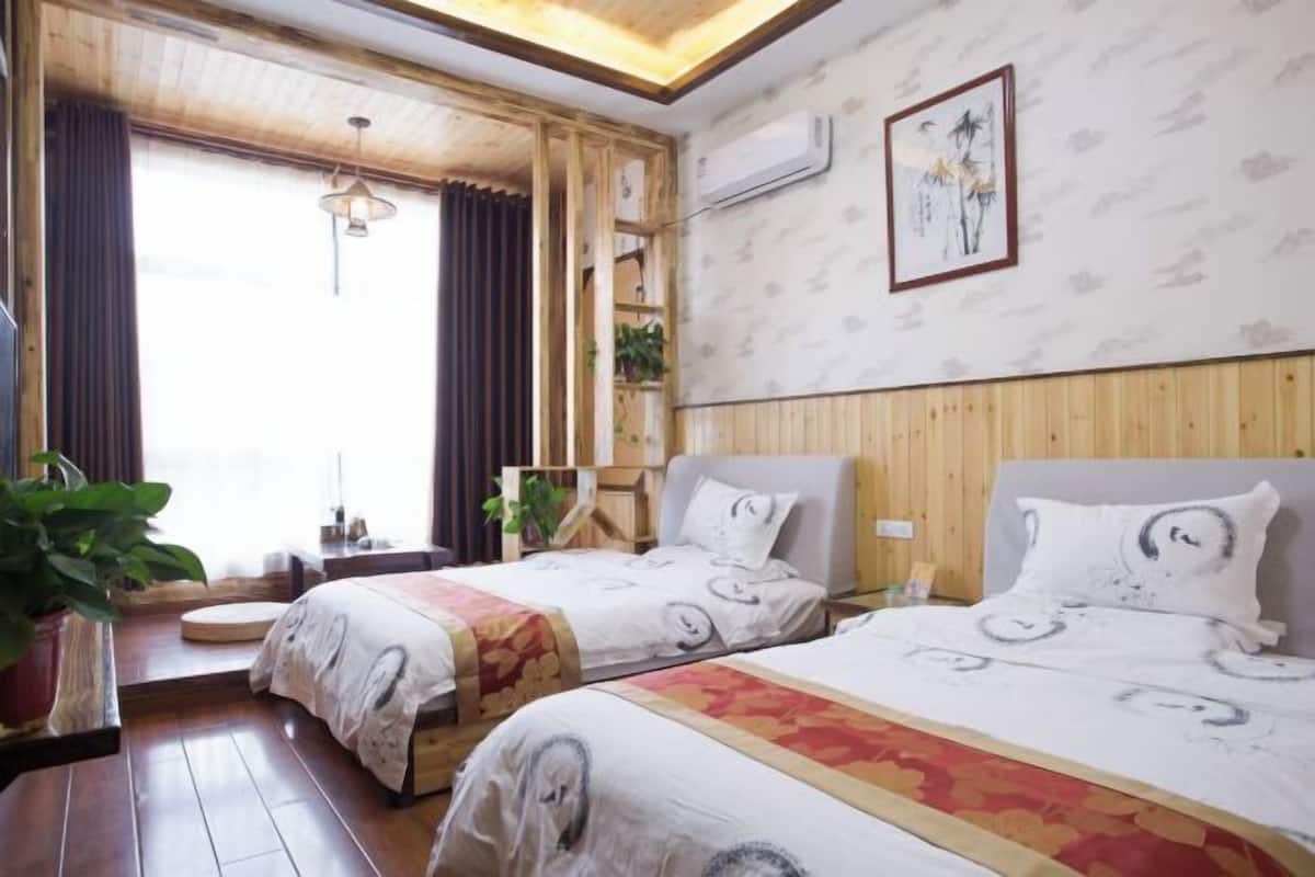 A hotel room with two beds, wooden paneling, a window with curtains, a wall-mounted air conditioner, and a framed artwork.