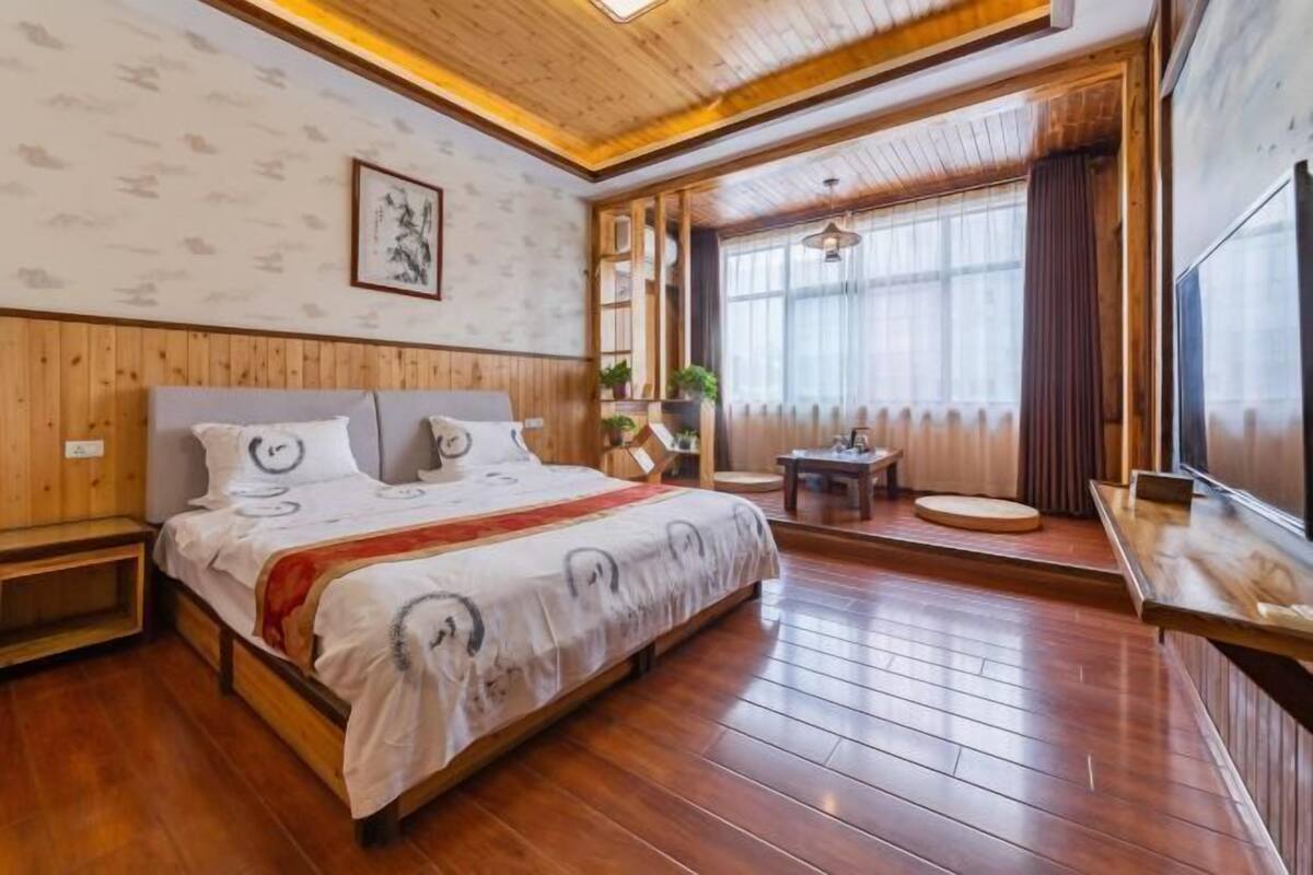A wooden-paneled bedroom with a bed, bedside tables, a small table, and a TV.