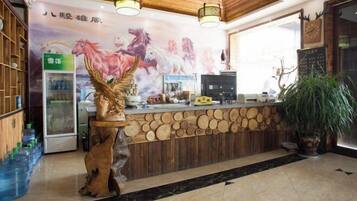 A reception area with a wooden counter, a decorative horse sculpture, a refrigerator, and a large window.