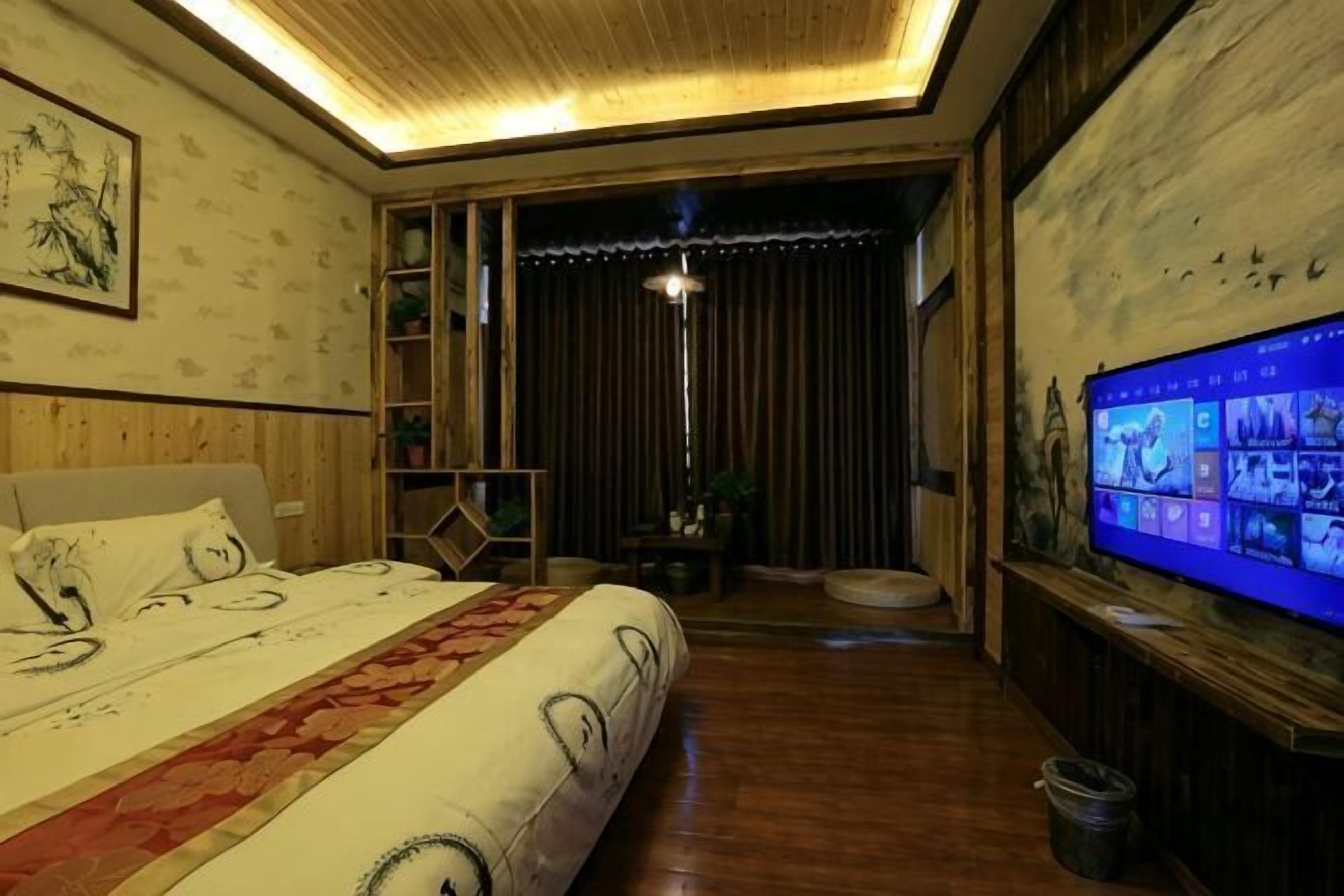 Een slaapkamer met een bed, een televisie, een plafondlamp en een raam met gordijnen.