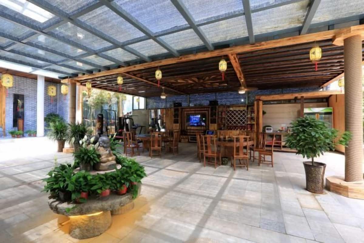 A spacious indoor area with a high ceiling, stone flooring, wooden furniture, and potted plants.