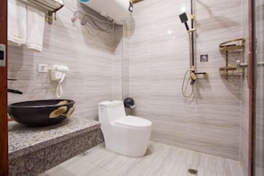 Un baño moderno con pared de mármol, inodoro blanco, lavabo tipo cuenco negro y cabezal de ducha de mano.