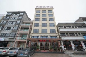 A multi-story building with a central entrance, several parked cars, and a clear sky. - Wenzhou Dongtou Overseas Chinese Hotel (Wenzhou)