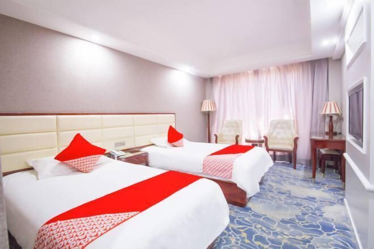 A hotel room with two beds, a desk, a chair, and a TV.