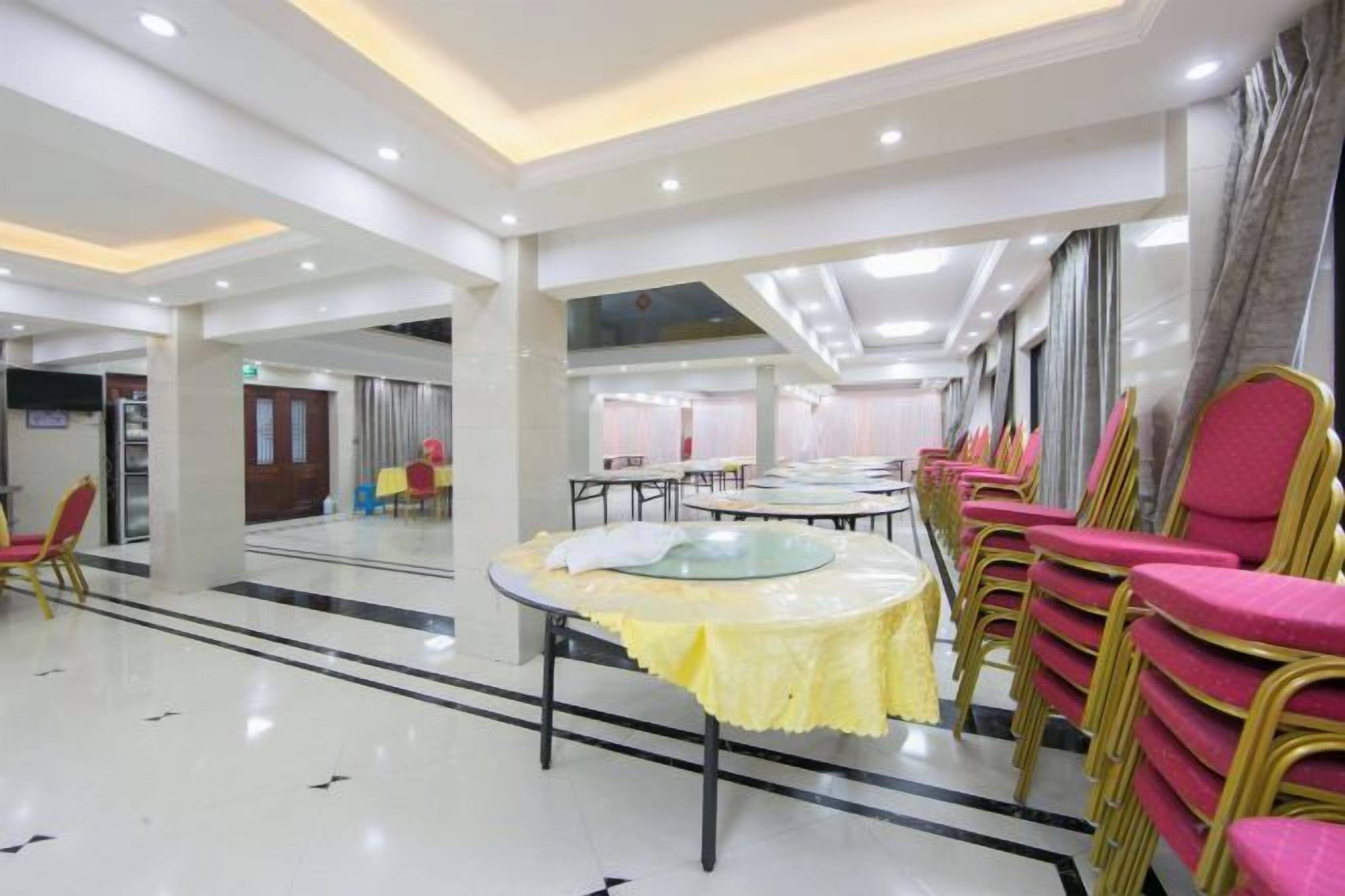 A spacious indoor area with tables and chairs arranged for dining, a high ceiling with recessed lighting, and a large window providing natural light.