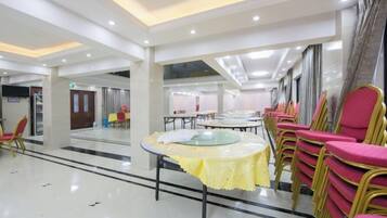 A spacious indoor area with tables and chairs arranged for dining, a high ceiling with recessed lighting, and a large window providing natural light.