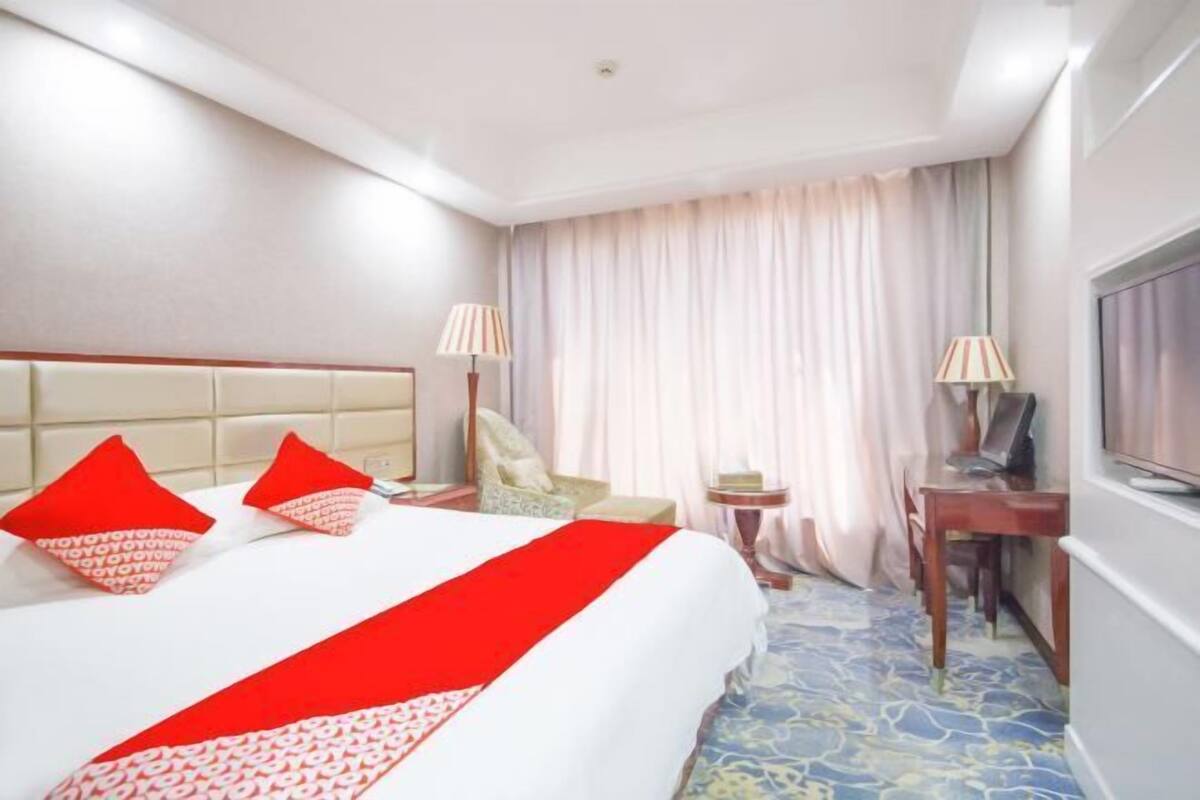 A hotel room with a large bed, two bedside lamps, a desk with a chair, and a television.