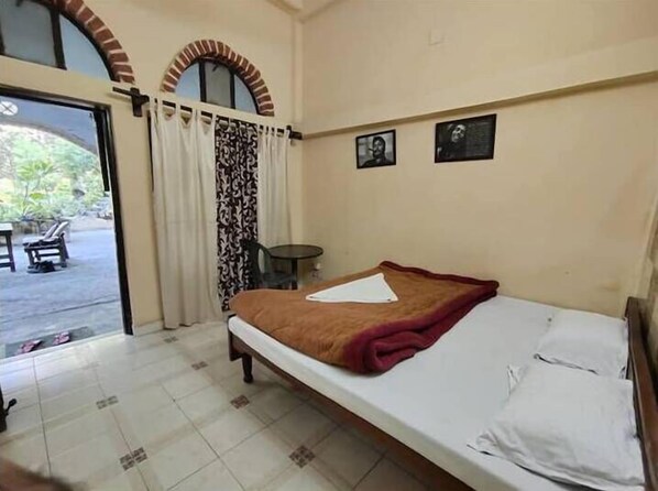 Une chambre avec un lit simple, donnant sur l’extérieur grâce à une porte vitrée, avec une petite table ronde et deux tableaux encadrés au mur.