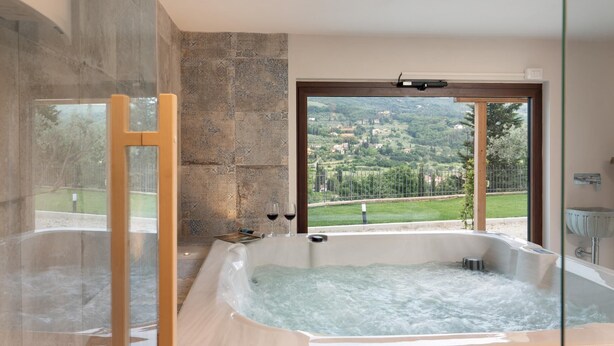 Un baño con una bañera grande, cabina de ducha con paredes de vidrio y vistas a un paisaje verde a través de una puerta.