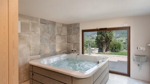 Ein modernes Badezimmer mit einer großen Badewanne, Steinwänden und Blick ins Grüne.