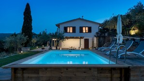 Una casa de dos pisos con piscina, mobiliario exterior y una pérgola.