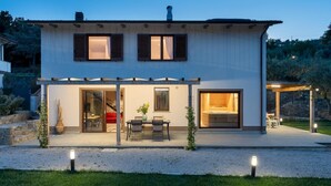 Una casa moderna de dos pisos con un porche cubierto, un comedor y un dormitorio visible.