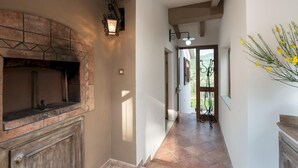Un pasillo con chimenea de piedra, una puerta que da al exterior y una ventana con flores amarillas.