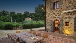 Ein Essbereich im Freien mit einem Steinhaus, einem Kiesweg und einem kleinen Haus im Hintergrund.