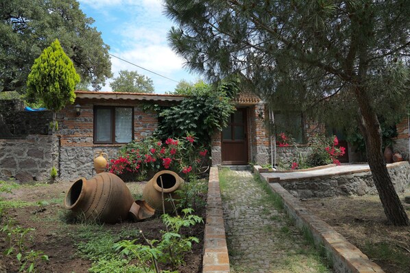 Une maison de campagne en pierre, avec un toit en tuiles, une porte en bois et un petit jardin agrémenté de plantes en pot et de fleurs.