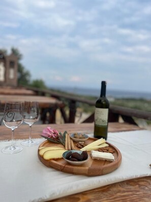 Una mesa de madera con una tabla de quesos, frutos secos y una botella de vino, frente a un paisaje pintoresco.