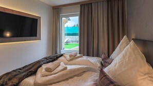 A hotel room with a bed, a flat-screen TV mounted on the wall, a window with curtains, and a view of the outside. - Accommodation with sauna near the ski lift (Mittersill)