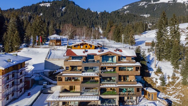 A multi-story wooden building with balconies, surrounded by snow-covered terrain and trees, likely a hotel or resort. - Accommodation with sauna near the ski lift (Mittersill)