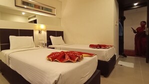 Habitació d'hotel amb dos llits, cadascun amb un llençol blanc i una manta vermella. Hi ha una taula de nit amb una làmpada, un telèfon i una taula petita. L'habitació té un disseny modern, amb un mirall gran sobre els llits i una porta que condueix a una altra habitació.