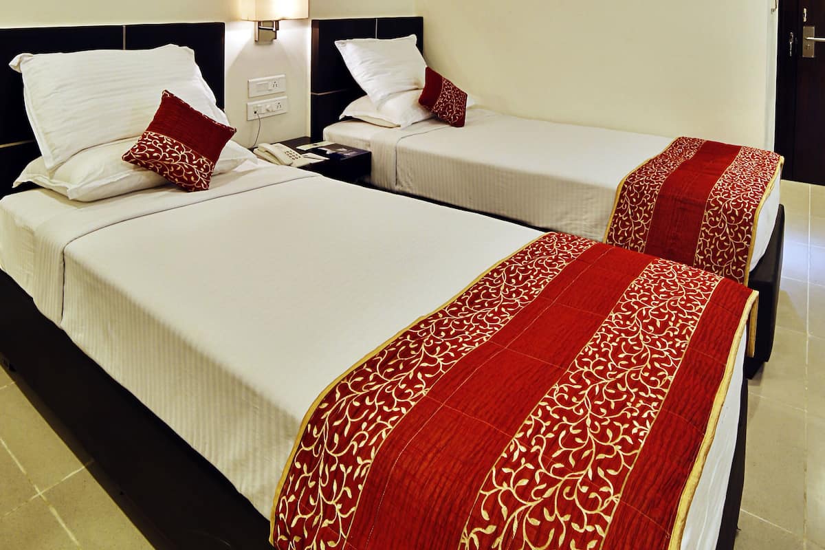 Quarto de hotel com duas camas, cada uma com colcha estampada em vermelho e dourado, travesseiros brancos e uma mesa de cabeceira com abajur.