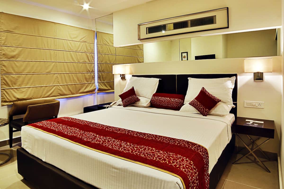Quarto de hotel com uma cama grande, ventoinha no teto, mesa de cabeceira com abajur e televisão fixada na parede.