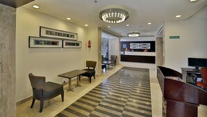 Un vestíbul d'hotel amb un paviment a escacs, zona de seients i una taquilla d'eixida.