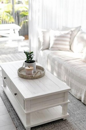 A white wooden coffee table with drawers, a potted plant, and a candle on a woven tray.
