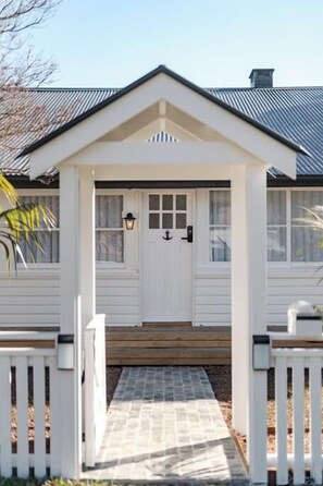 A white house with a front porch, a wooden deck, and a metal roof. - Steamers Bungalow (Huskisson)