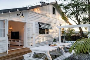 A white house with a patio area featuring a table and chairs, a television, and a striped awning.