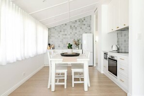 A modern kitchen with white cabinetry, a central island, and a dining area with a white table and chairs.