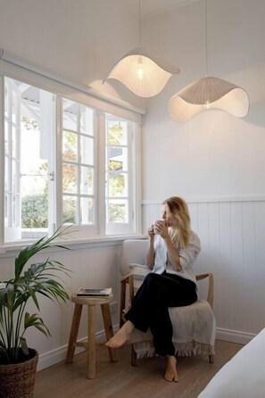 A room with a large window, a chair, a small table, and a hanging light fixture.