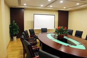 Uma sala de conferências com uma grande mesa oval, cadeiras pretas, uma tela de projetor e um vaso de planta.